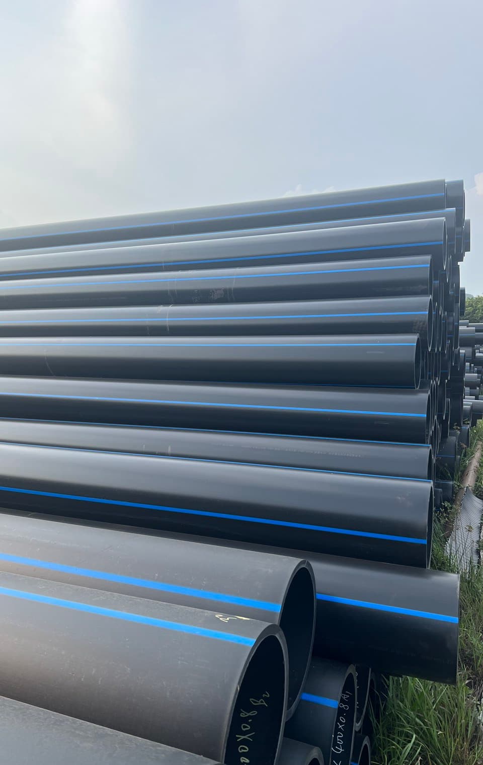Bundles of blue-striped and black PE pipe racked outdoors, the sizes used for field mains