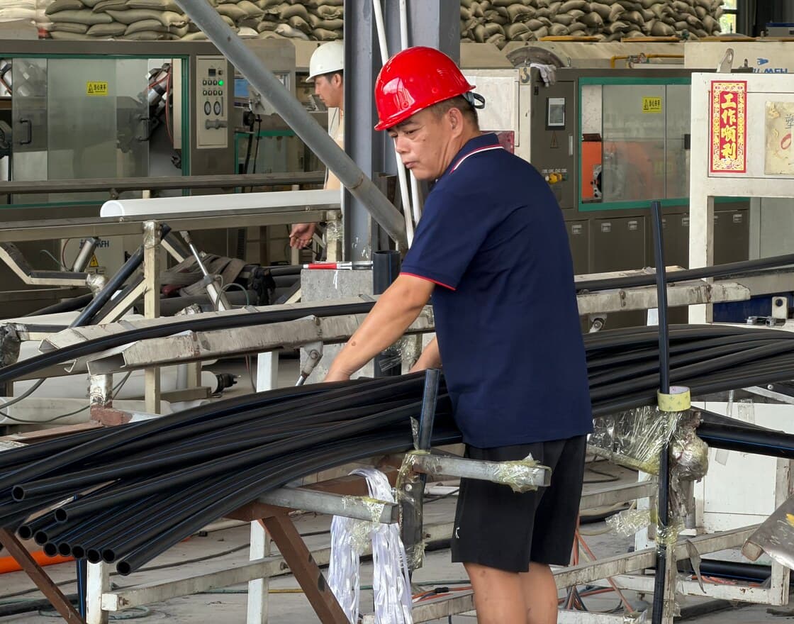An operator in a red hard hat feeding coiled HDPE pipe through the line