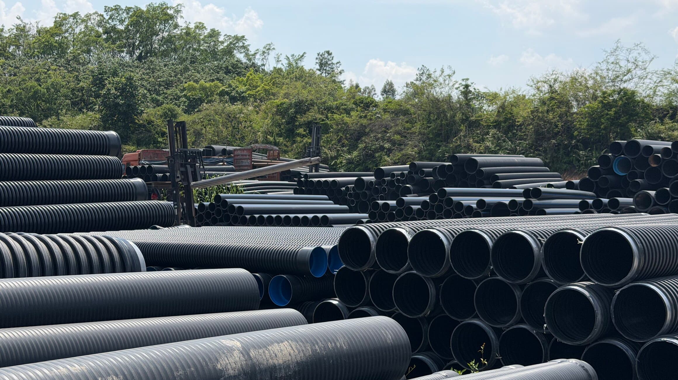 Black double-wall corrugated pipe stacked alongside solid wall pipe, sorted by diameter
