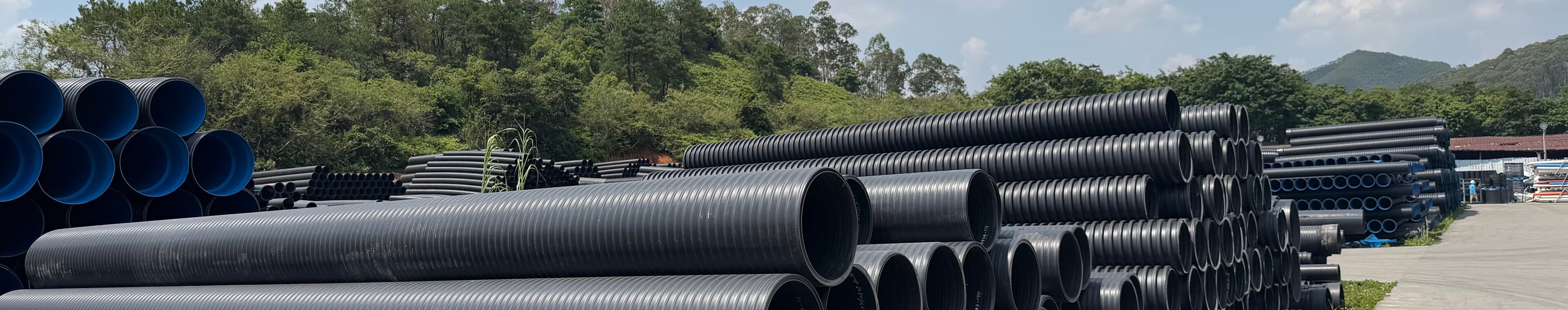 Double-wall corrugated sewer pipe stacked across the yard, sorted by diameter