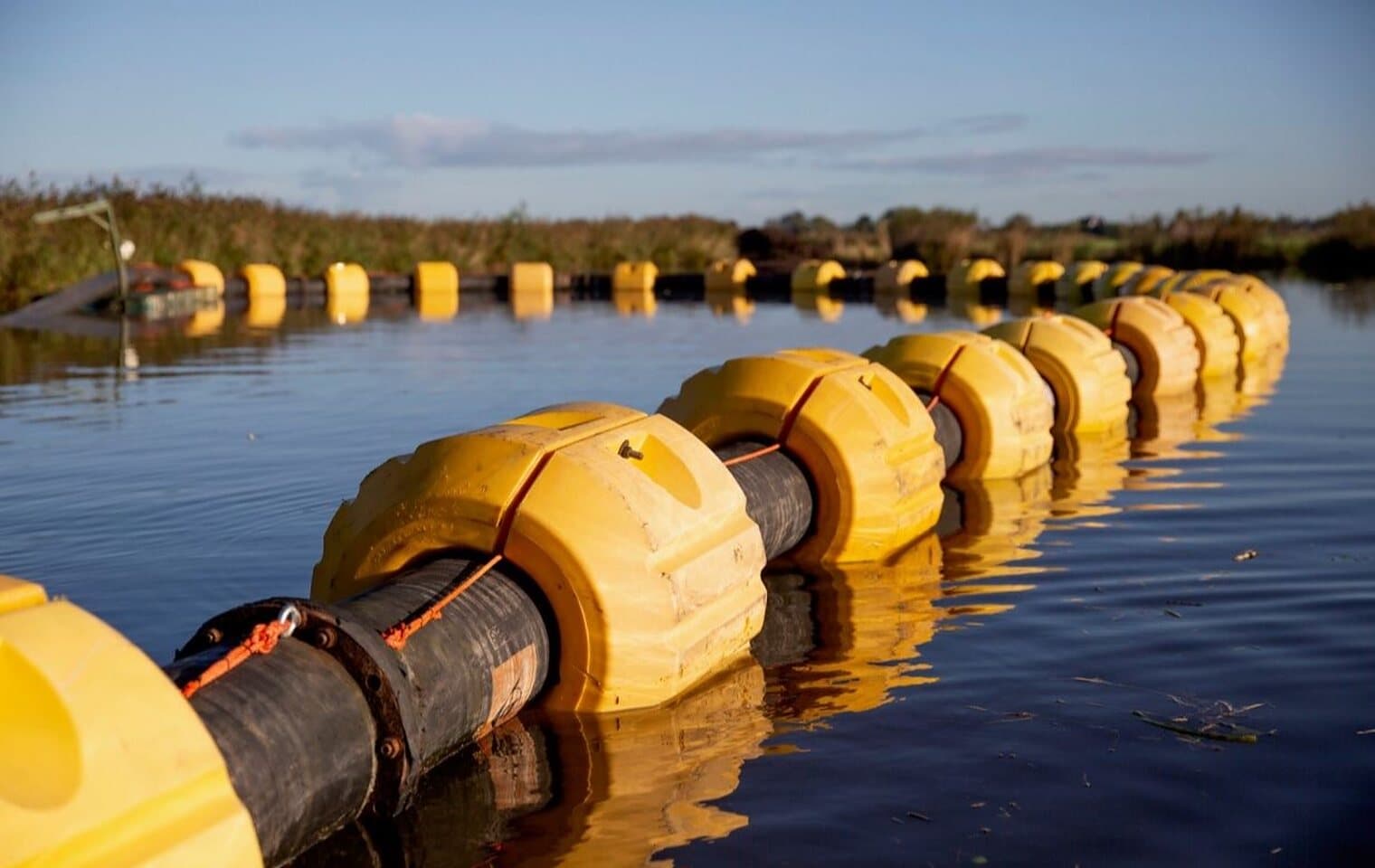 A dredging line afloat on the water, carried by clamped yellow pontoons