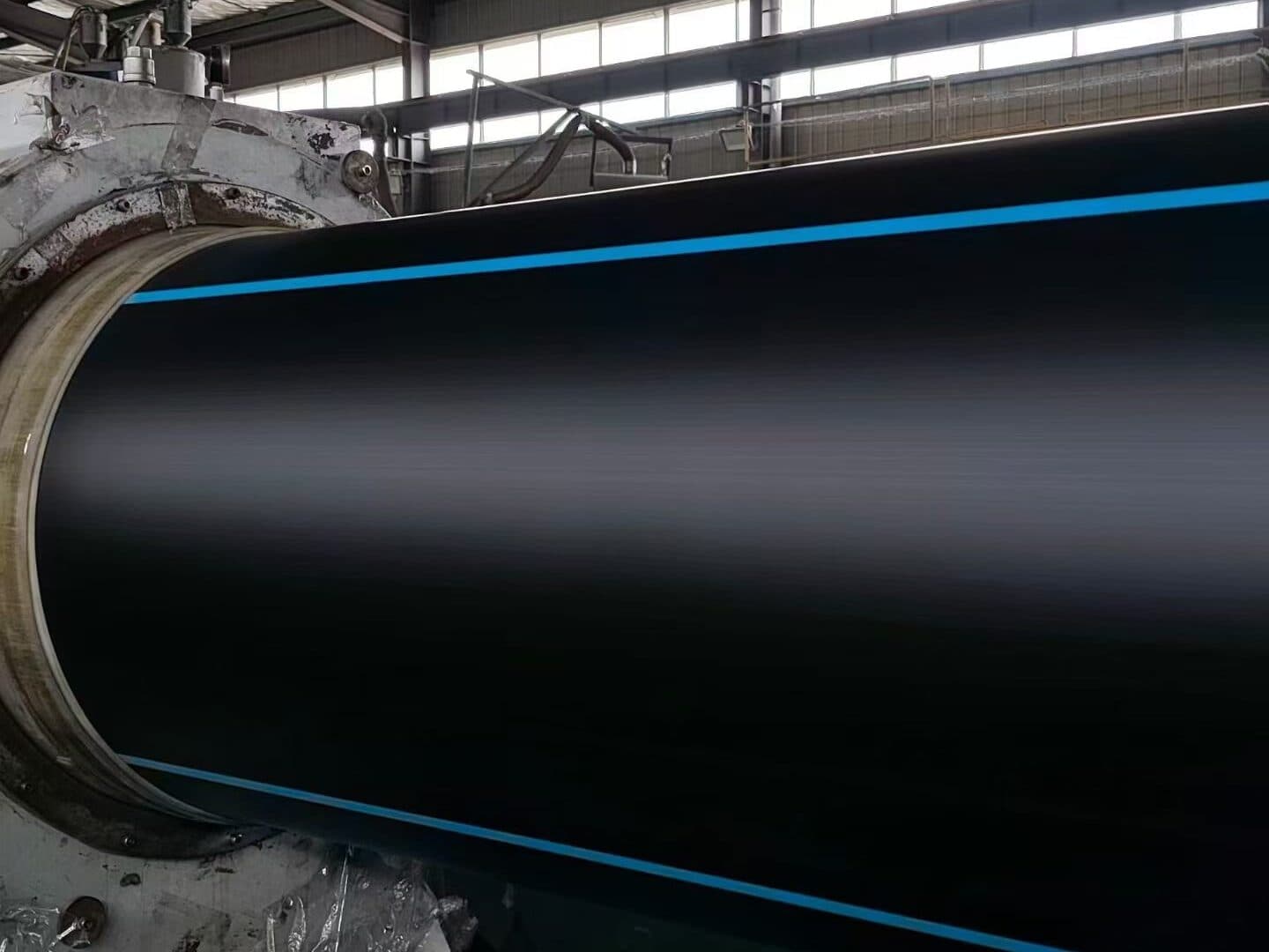 A large-diameter black PE100 pipe with blue stripes leaving the vacuum calibration tank on the extrusion line