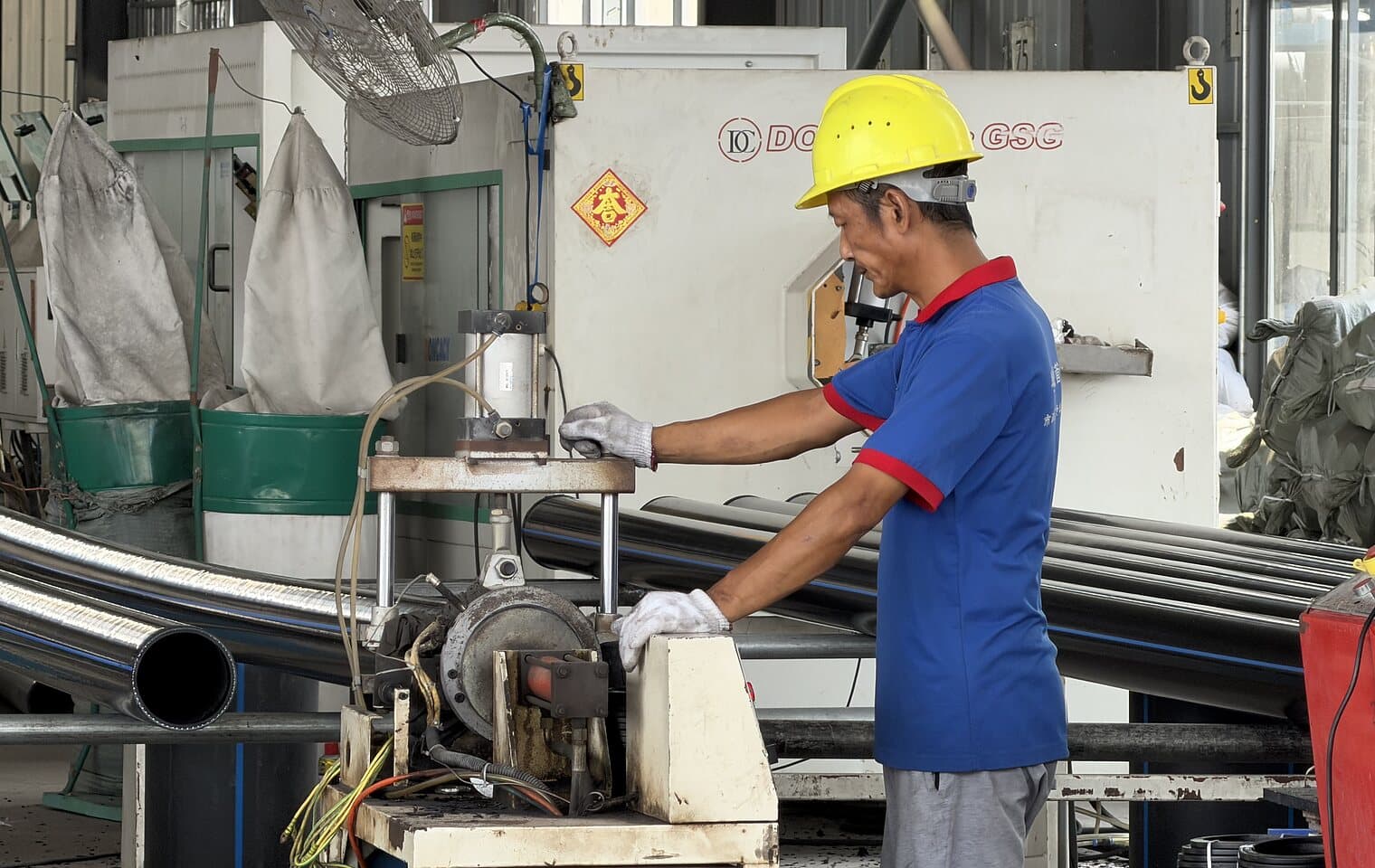 An operator in a hard hat working the cutting machine on the shop floor