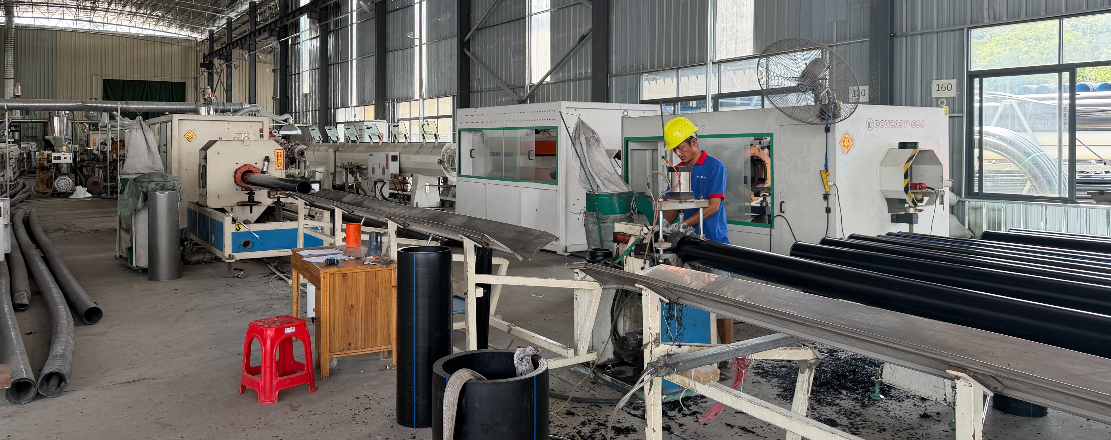 A worker at the cut-off saw on our HDPE pipe extrusion line, with black PE100 pipe on the racks alongside