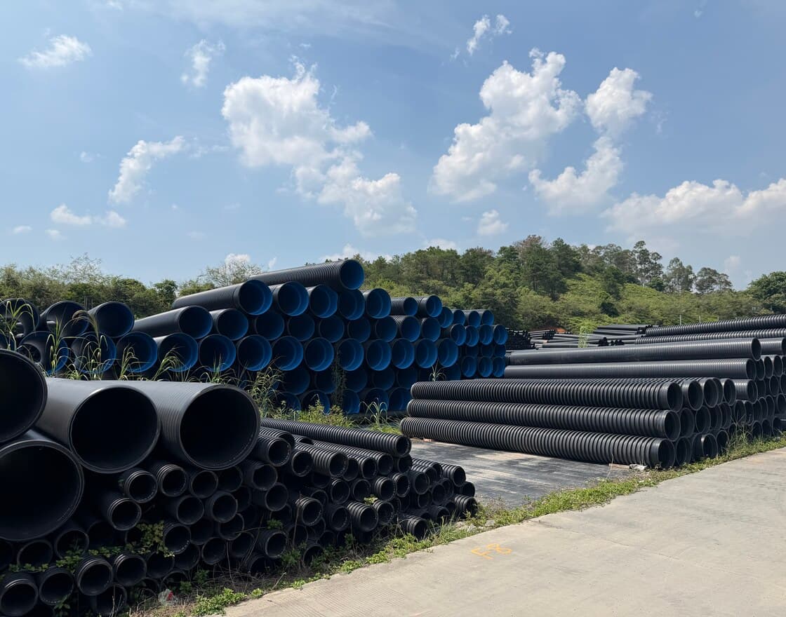 A wide view of the stock yard with blue-lined corrugated pipe and black PE100 pipe under an open sky