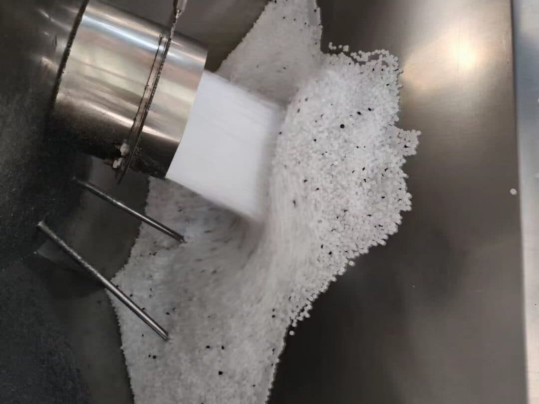 White PE100 compound granules with black masterbatch pellets pouring into the stainless-steel feed hopper