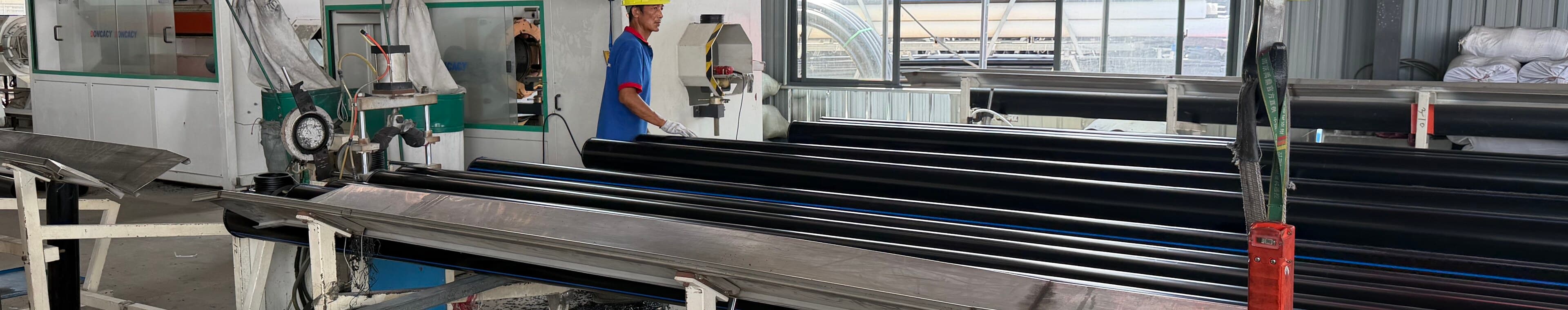 An operator in a yellow hard hat working alongside a run of PE100 pipe on the fabrication bench