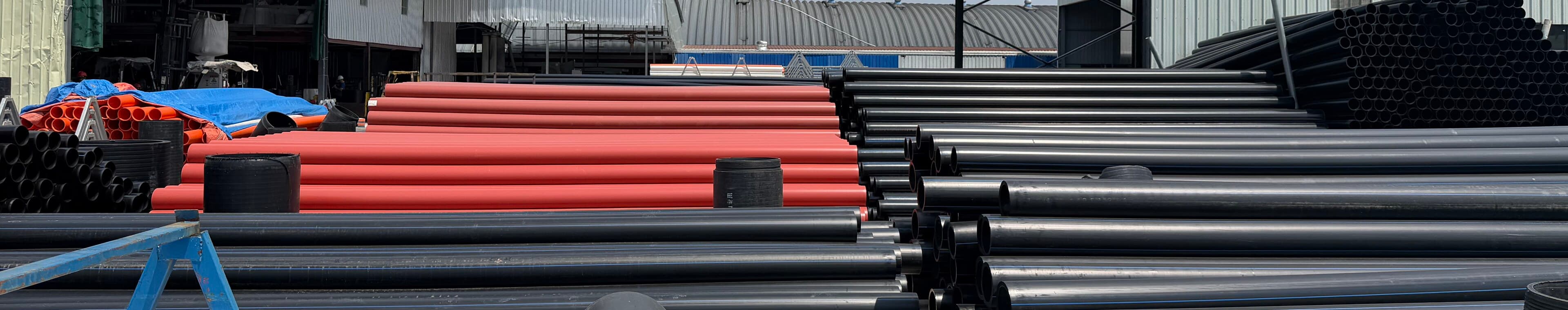 Rows of orange conduit and black PE100 pipe laid out on racks in the yard